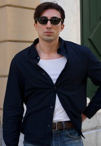 Schwarze Button-Up-Shirt über einem weißen Tanktop, kombiniert mit blauen Jeans und Sonnenbrille. Das Hemd hat eine Brusttasche und hochgekrempelte Ärmel.
