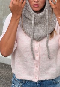Růžový pletený cardigan s krátkými rukávy a knoflíky, kombinovaný se šedým texturovaným šátkem s rolákem a šňůrkami.