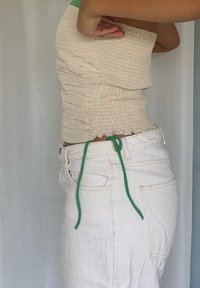 Un top tube crem cu pliuri, realizat dintr-un material elastic, asortat cu blugi albi cu talie înaltă, având un șnur verde la talie.