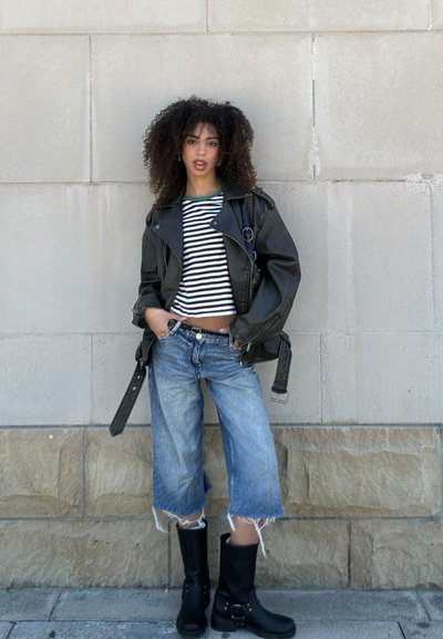 Chaqueta de moto de cuero negro, top corto a rayas, culottes de mezclilla desgastados de color azul claro, botas negras hasta la rodilla con hebillas.