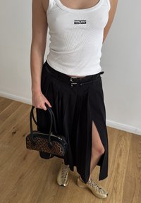 Saia preta plissada com uma fenda alta, top de tanque branco com relevo, bolsa de estampado de leopardo e ténis bege com atacadores.