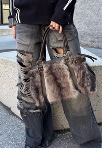 Brązowa skórzana torebka z futrzanymi akcentami, podwójnymi uchwytami i złotymi elementami. Noszona z przetartymi szarymi dżinsami z dużymi rozcięciami.