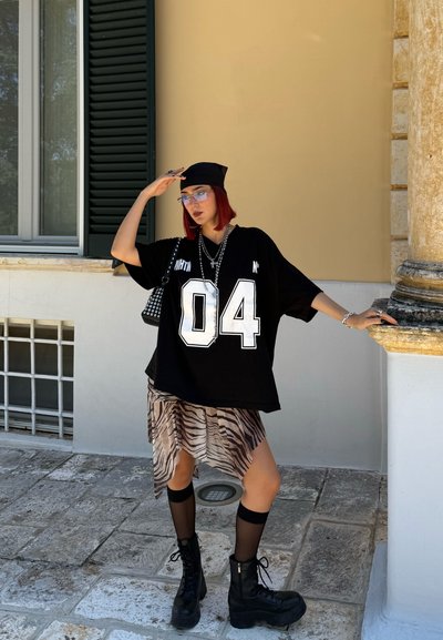 Camiseta negra oversize con estampado blanco "04", falda asimétrica de estampado de cebra, medias hasta la rodilla y botas de combate negras. Gafas y accesorios visibles.