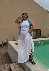 Denim vest over en hvit tank top og en lagdelt maxiskjørt. Svart og hvit mønstrete kne-høye støvler. Stående ved en basseng på tre-dekk.