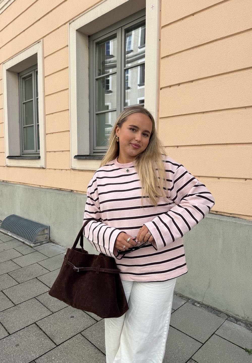 Lyserød og sort stribet sweatshirt med lange ærmer, kombineret med brede hvide bukser og en mørkebrun ruskindstaske.