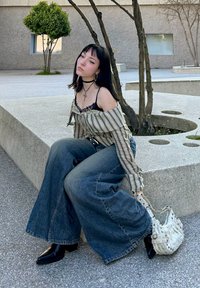 Ριγέ μπλούζα με ανοιχτούς ώμους και δαντέλα στην άκρη, συνδυασμένη με φαρδιά τζιν παντελόνια σε μπλε απόχρωση. Μαύρες μπότες αστραγάλου και λευκή τσάντα με υφή με διακοσμητικά στοιχεία.