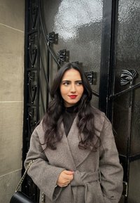 Grå wool-blend frakke med en omslagdesign, brede ærmer og en bælte i taljen. Sammen med en sort top og en taske med kæde-strop.
