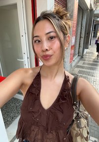 Brun rynkete halterneck topp med dyp V-hals. Brukes med en mønstret håndveske med lærrem. Naturlig setting med utendørs fortau.