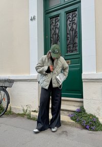 Veste matelassée verte clair, haut noir à manches longues, pantalon large à rayures noires, chaussures argentées métalliques et casquette verte avec logo.