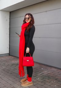 Sac à main rouge, body noir, écharpe rouge, leggings noirs, chaussettes rouges, chaussures beiges. Texture lisse, design géométrique sur le sac à main, motif tartan sur les chaussures.