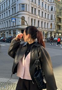 Svart läderjacka över en rosa ribbad cardigan, accessoriserad med stora hoops och en svart kviltad väska, hår i hästsvans.