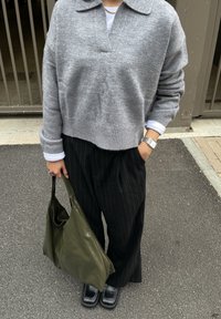 Suéter de cachemira gris con cuello de solapa, combinado con pantalones negros de rayas finas y corte amplio. Sosteniendo un bolso tote verde oliva, y calzando zapatos negros.