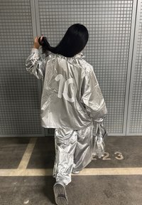 Sølv tracksuit med reflekterende materiale, løstsiddende top og bukser, med nummer 10 i hvidt på ryggen, parret med matchende fodtøj.