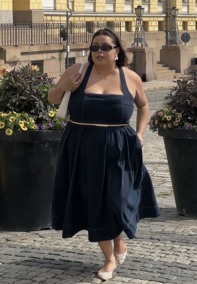 Vestido de mezclilla con escote cuadrado, silueta en A, color marino y cinturón color marrón claro. Llevado con bailarinas de encaje y gafas de sol.