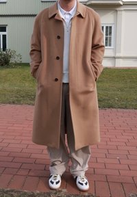 Teddybruine wollen jas met een notch-kraag, enkel-gebuton design en vier knopen; gecombineerd met lichtbeige broek en witte sneakers.