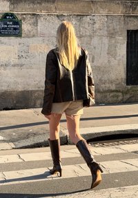 Barna bőrdzseki, bézs rövidnadrág és barna, térd fölé érő, magassarkú csizma. A dzseki textúrázott felületű; a rövidnadrág feszített szélekkel rendelkezik.