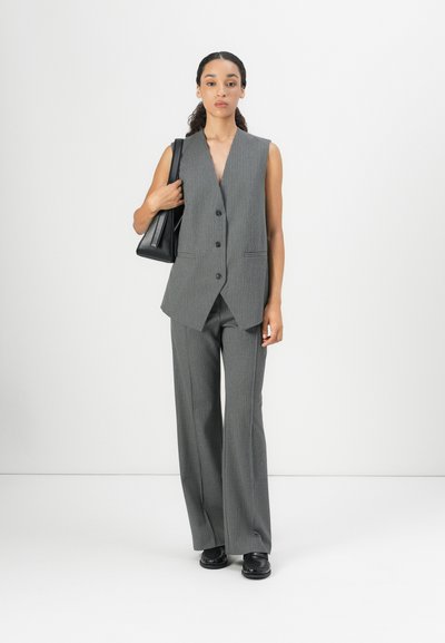 Chaleco sin mangas a rayas gris y pantalones de pierna ancha, acompañados de un bolso negro y zapatos, todo sobre un fondo blanco liso.