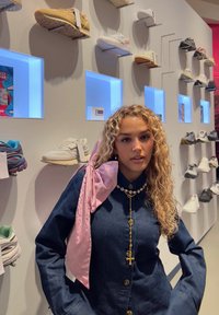 Jeanshemd mit langen Ärmeln und Knopfleiste, ergänzt durch einen pinkfarbenen Satin-Schal. Ausstellung verschiedener Sportschuhe auf einer hellen Wand.