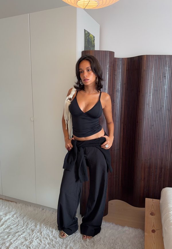 Young woman in black top and wide black pants stands on white rug in modern room with wooden divider and white wardrobe.