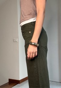 Pantaloni in velluto a coste verdi con tasche laterali, abbinati a una maglietta aderente beige. Un bracciale in oro lucido, curvato, adorna il polso.