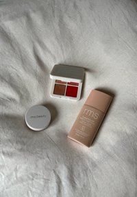 RMS Beauty cosmetica: een witte multi-kleur palette met twee rode en twee bruine tinten, een witte compact en een beige serumfles.