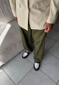 Μπεζ σακάκι, χαλαρές ελιές παντελόνες και καφέ παπούτσια με λευκές λεπτομέρειες. Λείες υφές και δομημένα σχέδια. Ουδέτερη παλέτα χρωμάτων.