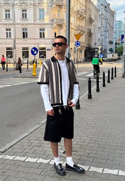 Camisa de rayas negras y crema de manga corta sobre una blusa blanca de manga larga, pantalones cortos negros, calcetines blancos, zapatos negros brillantes, accesorio de llavero.