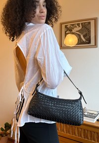 Black woven leather handbag with a curved shape and a single adjustable shoulder strap, displayed against a light background.