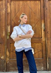 Λευκή φόρμα τοποθετημένη πάνω από πουκάμισο με μπλε και λευκές ρίγες, συνδυασμένη με σκούρα μπλε τζιν και κρατώντας μια μικρή τσάντα. Χρυσό ρολόι και σκουλαρίκια.