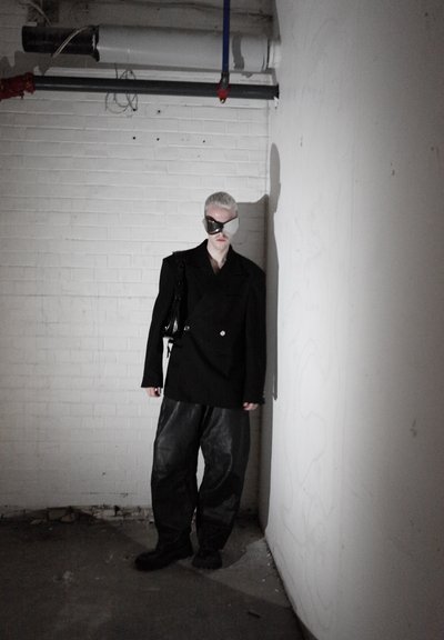 Blazer negro de gran tamaño con dobles botones, combinado con pantalones de cuero negros holgados. Unas gafas elegantes de color plateado y un bolso negro completan el conjunto.