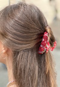 Clip per capelli floreale rosso realizzato in materiale lucido, con piccoli fiori in rilievo e foglie verdi, che tiene su capelli castani scuri in uno stile arrotolato.