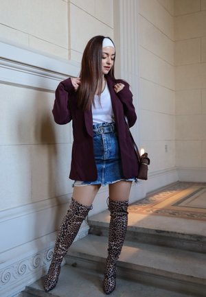Blazer burdeos sobre una blusa blanca, combinado con una falda de denim deshilachada. Botas de estampado de leopardo hasta la rodilla y un bolso marrón completan el look.