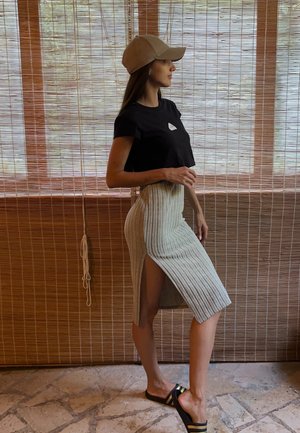 Camiseta negra corta con un pequeño logo, falda lápiz de punto ribeteada color beige con abertura lateral y sandalias negras con rayas doradas.