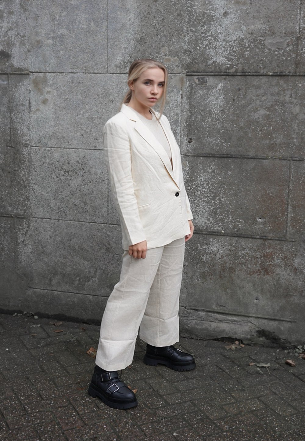 Blazer en lin beige avec un pantalon large assorti, présentant un bouton noir. Associé à des bottes à talons épais noires avec des boucles.