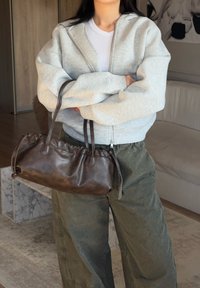 Felpa zip a grigio chiaro, top fitted bianco, pantaloni baggy oliva e una piccola borsa in pelle marrone scuro con dettagli arricciati e due manici.