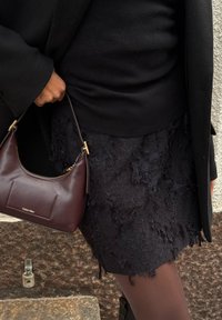 Fustă neagră texturată cu margini desfăcute, combinată cu un top negru și o geantă de umăr din piele burgundy cu detalii din aur.
