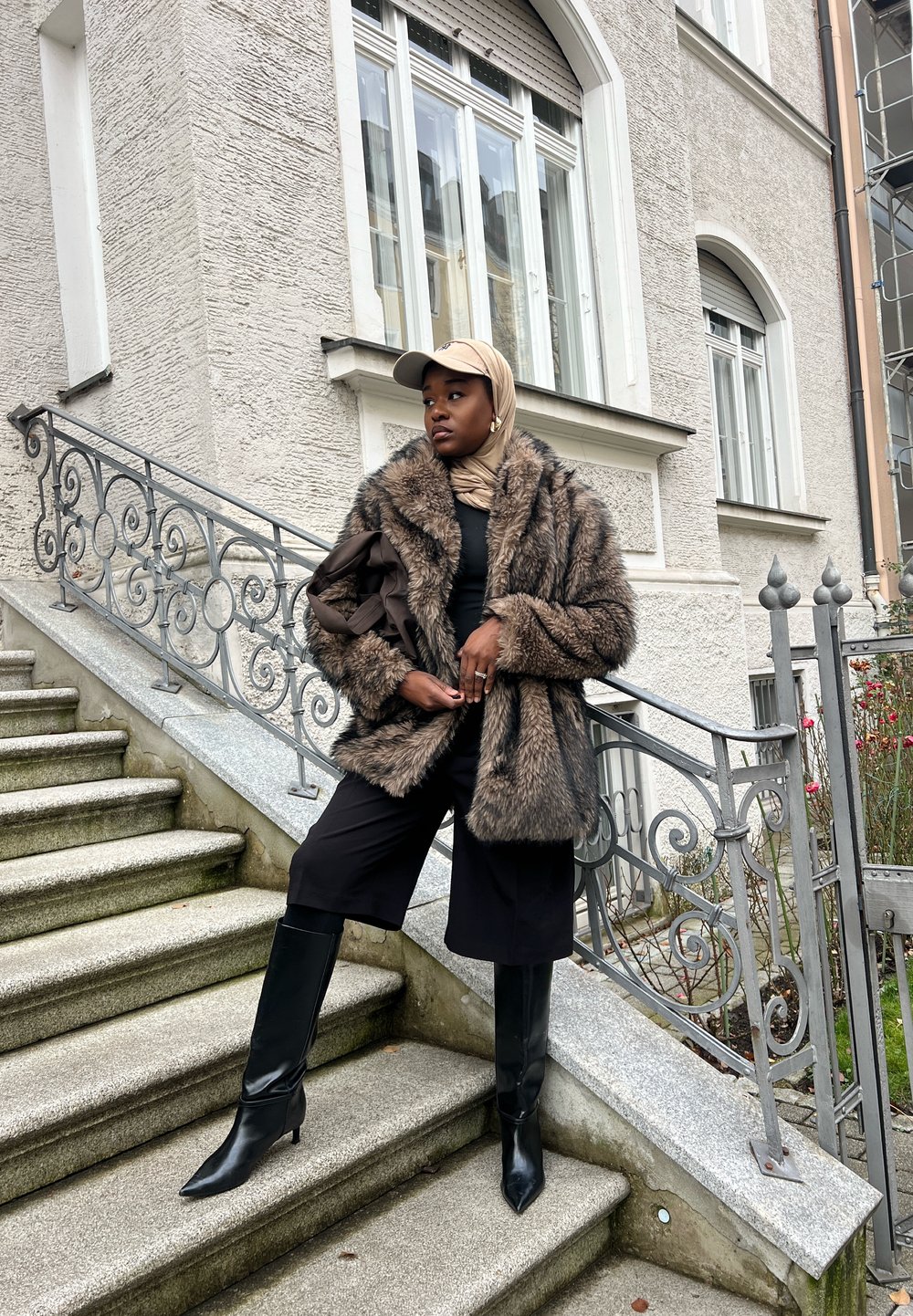 Barna szőrmekabát sállal ellátott gallérral, fekete felső és bőszárú fekete rövidnadrág. Fekete térd fölé érő csizma hegyes orral. Sapka és bebugyolált fejkendő.