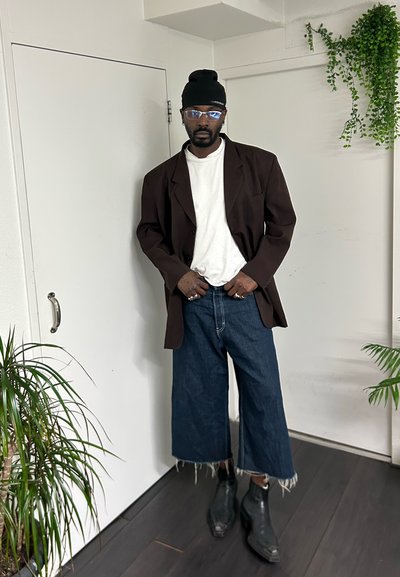 Blazer marrón de gran tamaño sobre una camiseta blanca, combinado con jeans azul denim recortados con dobladillos deshilachados y botines de cuero negro.