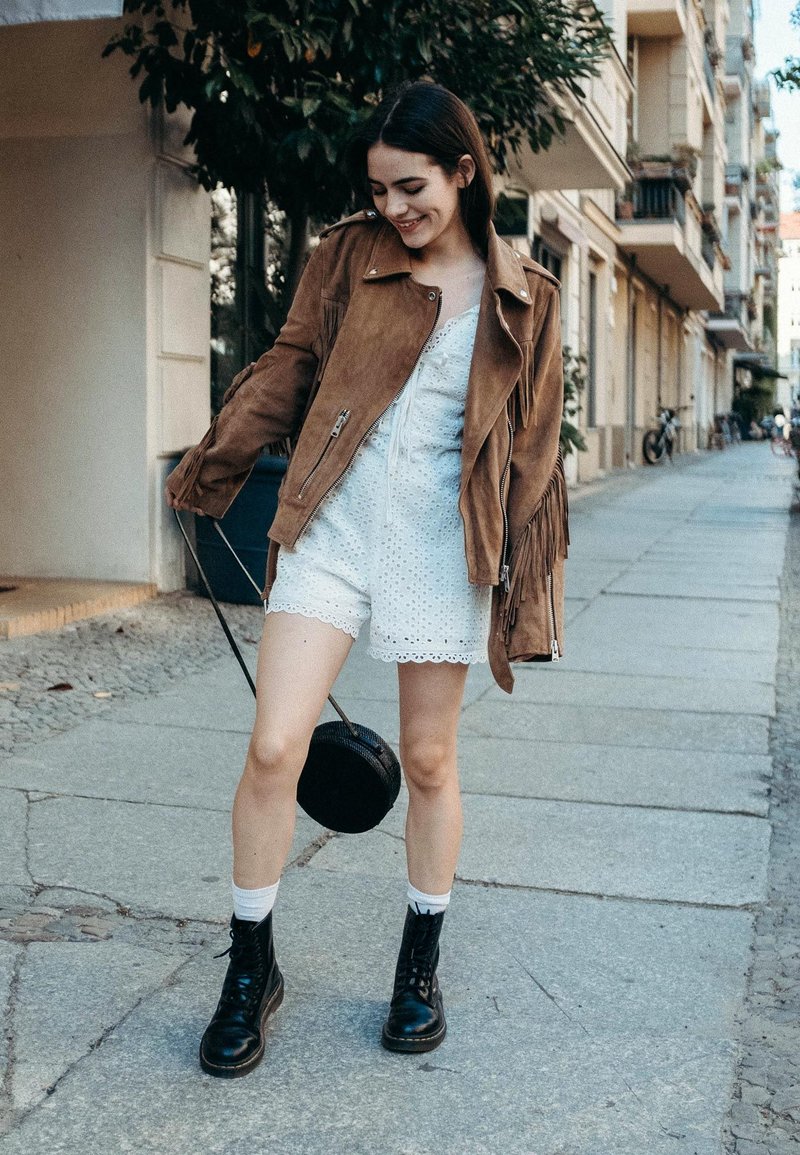 Barna velúr fringerdzseki, fehér horgolt sort csipkés szegéllyel, fekete katonai bakancs és egy kerek fekete keresztpántos táska. Járda háttér.