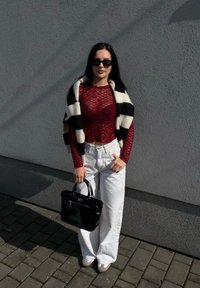 Κόκκινο δαντελωτό τοπ με μακριά μανίκια, επικαλυμμένο με μαύρο και άσπρο ριγέ κασκόλ, συνδυασμένο με άσπρα παντελόνια με φαρδιές γραμμές και μαύρη τσάντα.