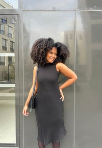 Svart ärmlös klänning med en något strukturerad yta, figurnära siluett och knälång fåll. I sällskap av en liten axelväska.