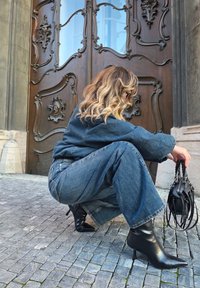 Laiade lõikega sinised teksapüksid, mida kantakse koos tumeda kampsuniga, täiustades seda põlveni ulatuvate mustade stiilsete kontsadega ja väikese musta õlakotiga.