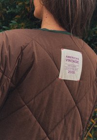 Barna steppelt dzseki, amelynek címkéjén a következő felirat áll: "AMERICAN VINTAGE 2005." Texturált felülettel rendelkezik, és kontrasztos zöld díszítés díszíti a gallért.