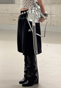 Șorturi negre Adidas cu dungi albe, geantă metalică argintie și cizme negre din piele până la genunchi. Topul are buline.