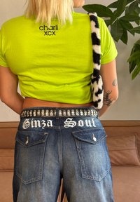 Neon zelena skrajšana majica s potiskanim besedilom na hrbtu, kombinirana z temno modrimi jeans hlačami z belim vezenjem in okrasnim pasom s studenčki.