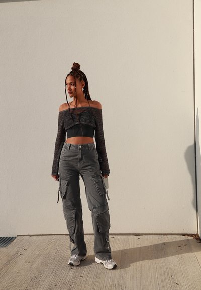 Top de punto gris sin hombros combinado con pantalones cargo grises con bolsillos, llevado con zapatillas deportivas blancas. El conjunto resalta la textura y las capas.