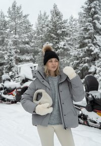 Giacca a vento grigia isolata con cappuccio, guanti in maglia crema e un maglione grigio chiaro, ambientati in un paesaggio innevato con motoslitte.
