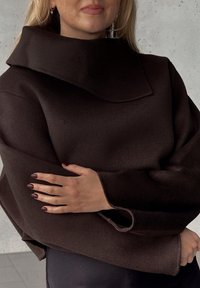 Brun oversized pullover med hög krage, tillverkad av mjukt, texturerat tyg. Har vida ärmar och uppvikta ärmslut. Snygg design.