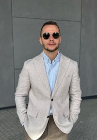 Svijetlosmeđi laneni sako preko svijetloplavog košulje s dugim rukavima, u kombinaciji s smeškim hlačama. Tamne okrugle sunčane naočale upotpunjuju izgled.