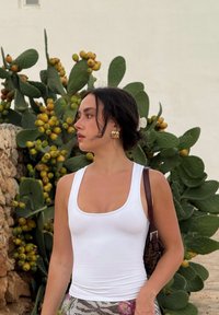 Top aderente bianco, gonna a fantasia e borsa marrone, con uno sfondo di piante di cactus verde e frutta gialla.